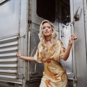 Emily Ann Roberts in a gold dress stepping off a train